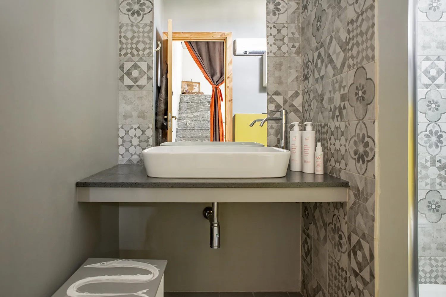 A bathroom vanity with a rectangular sink and patterned tile walls.