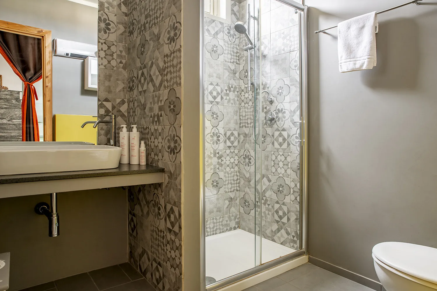 A bathroom with a patterned tile shower and a sink beside it.