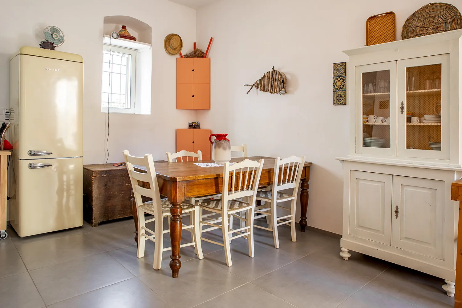 A dining area with a wooden table and chairs beside a refrigerator and display cabinet.