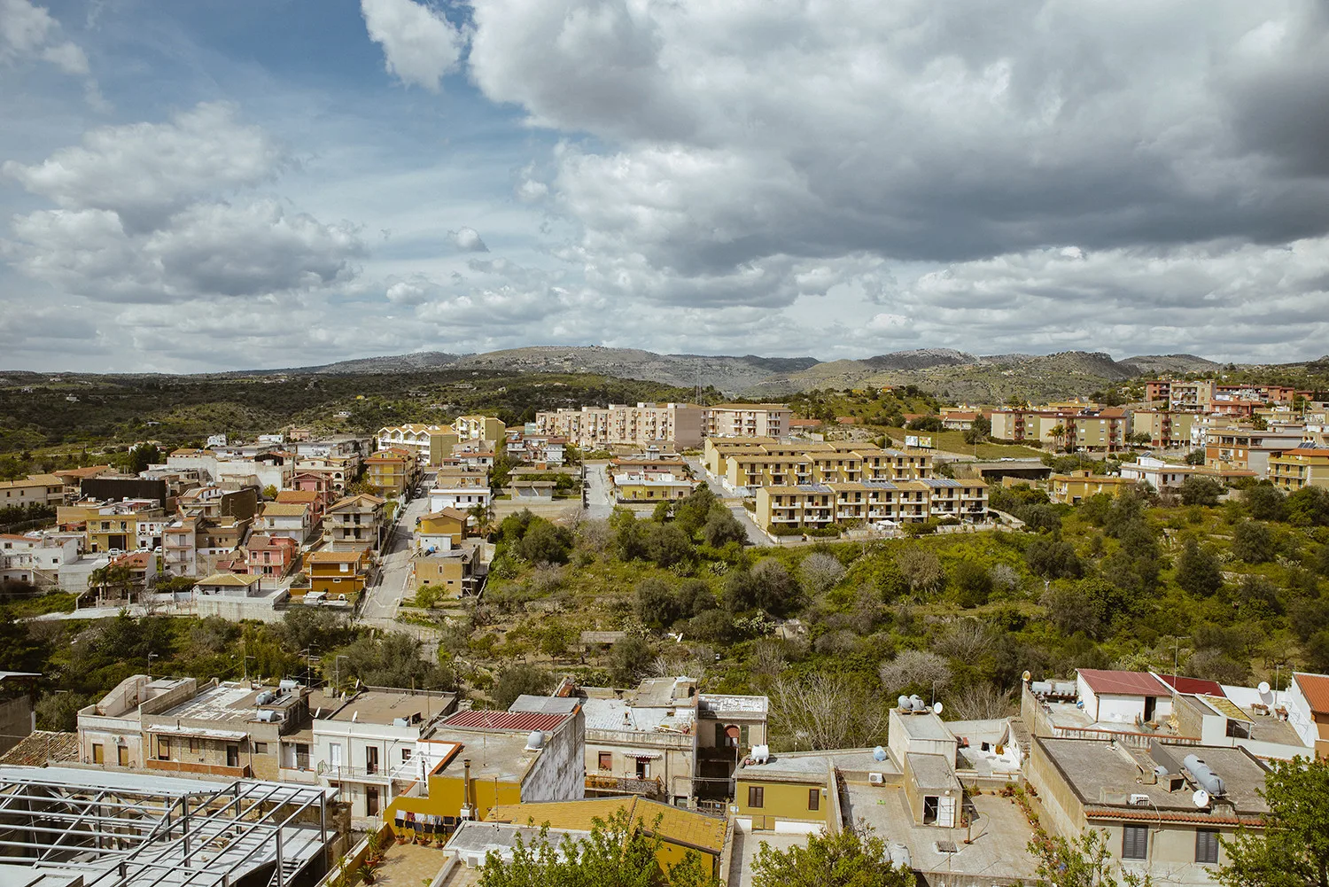 A town spreads across a hilly landscape beneath a cloudy sky.