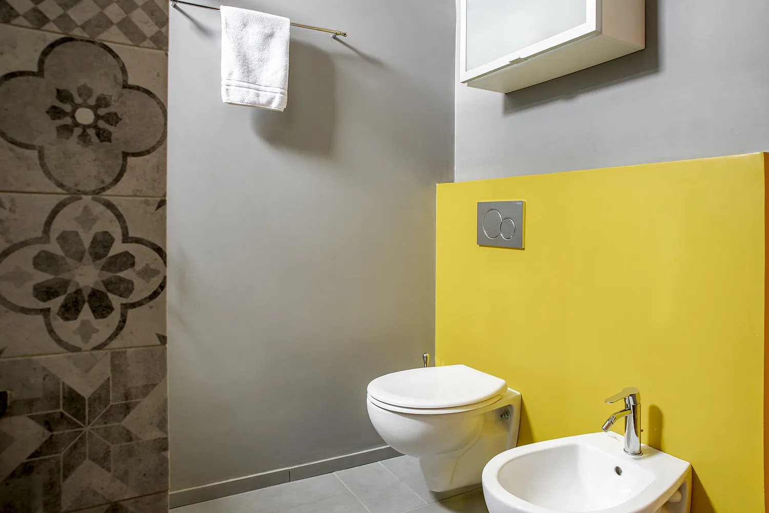 A bathroom with a toilet, bidet, and patterned tile wall.