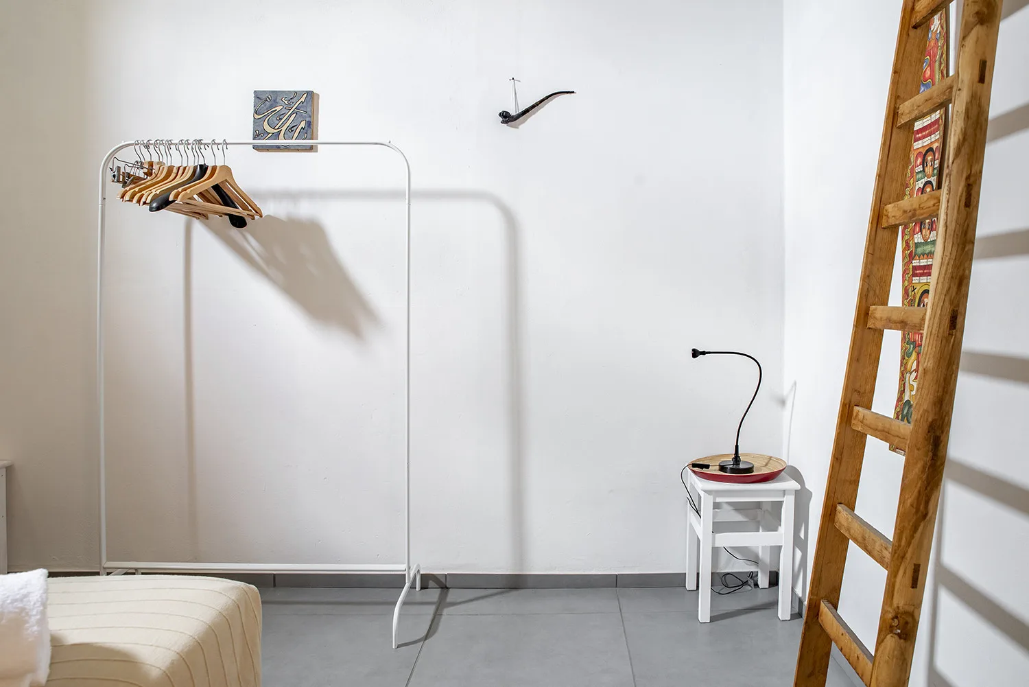A bright room features a clothing rack with hangers and a wooden ladder.
