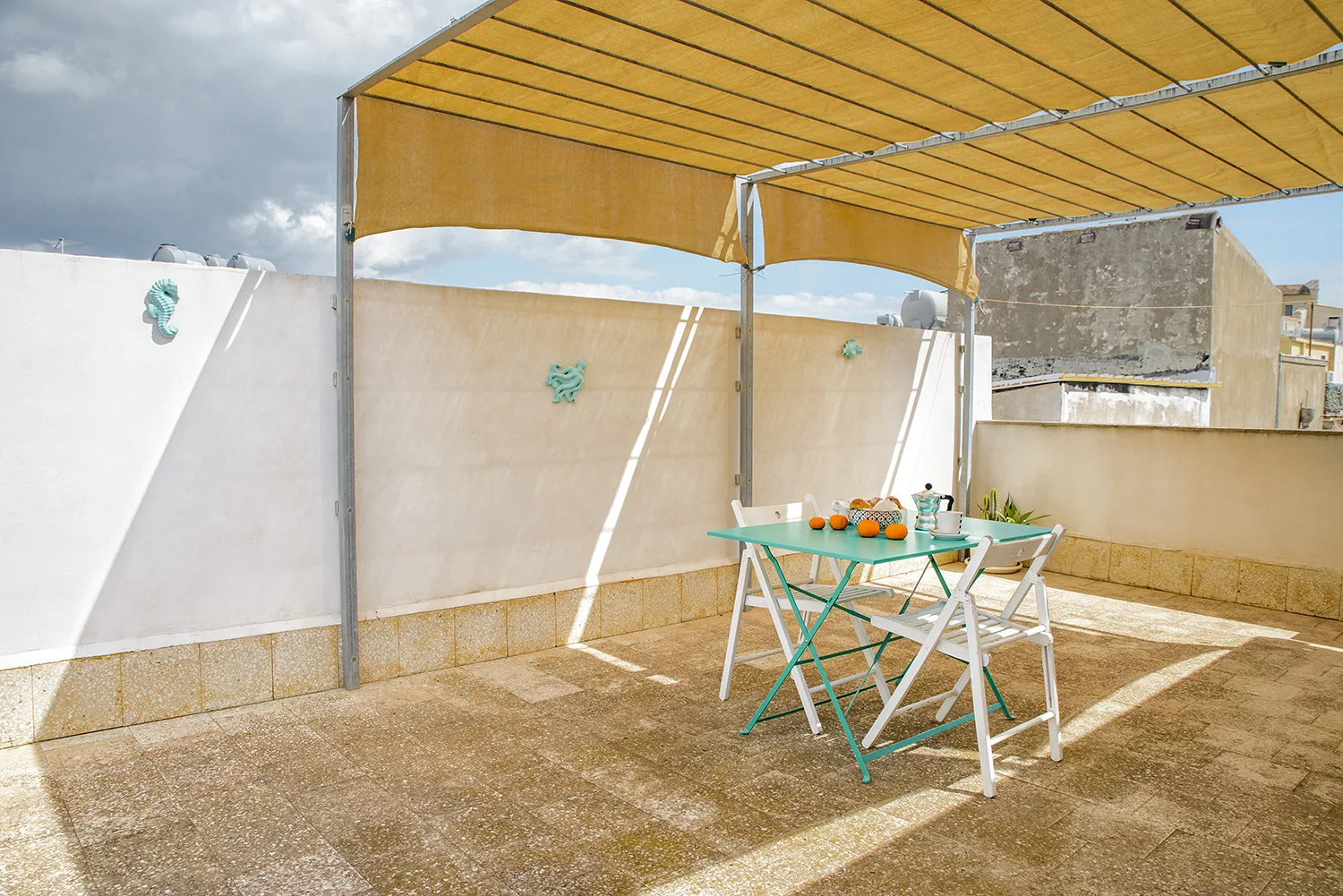 A sunlit rooftop terrace with a table beneath a yellow canopy.