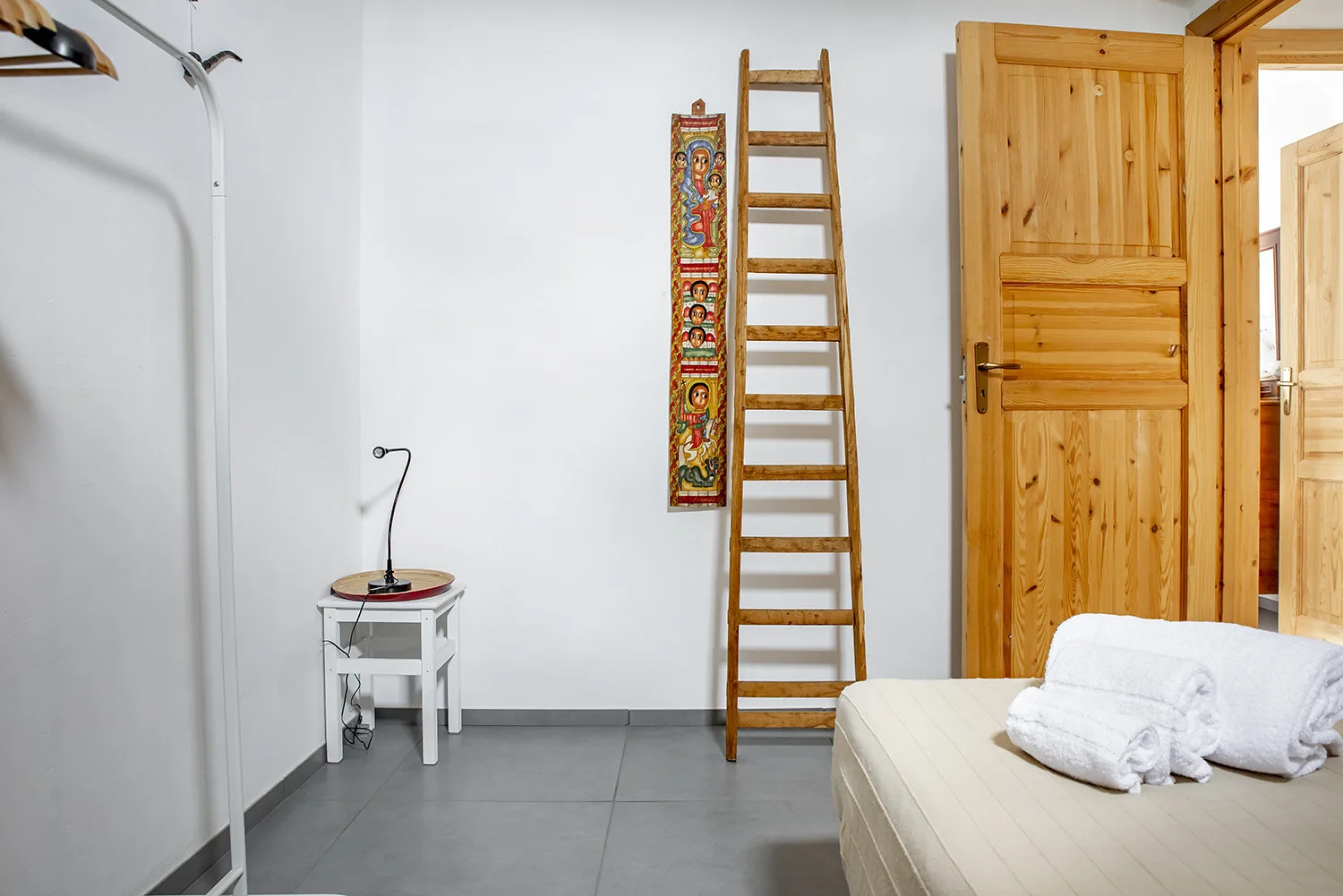 A bright room with a wooden ladder, colorful wall hanging, and bed.