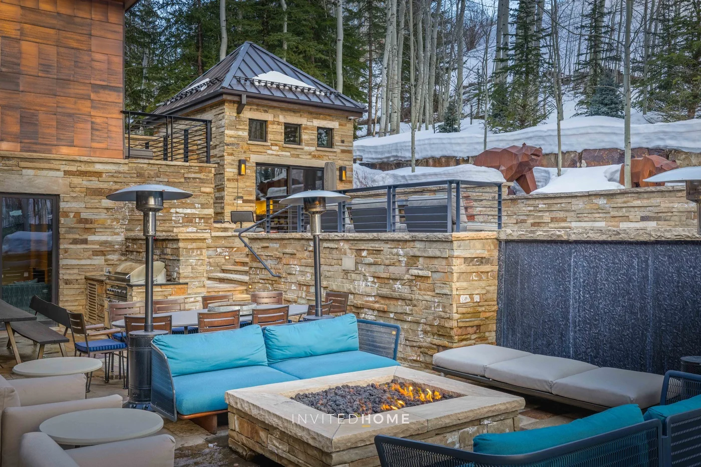 Un patio exterior con asientos acolchados, un muro de piedra y una fogata.