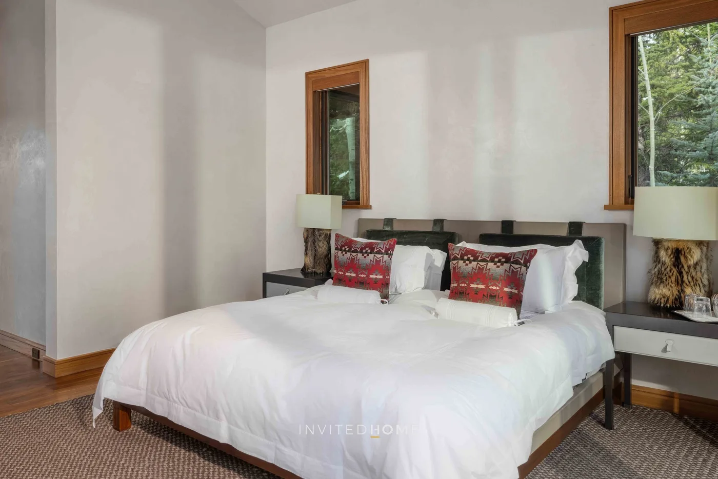 Dormitorio con una cama grande vestida con ropa blanca y ventanas con vistas a la vegetación.