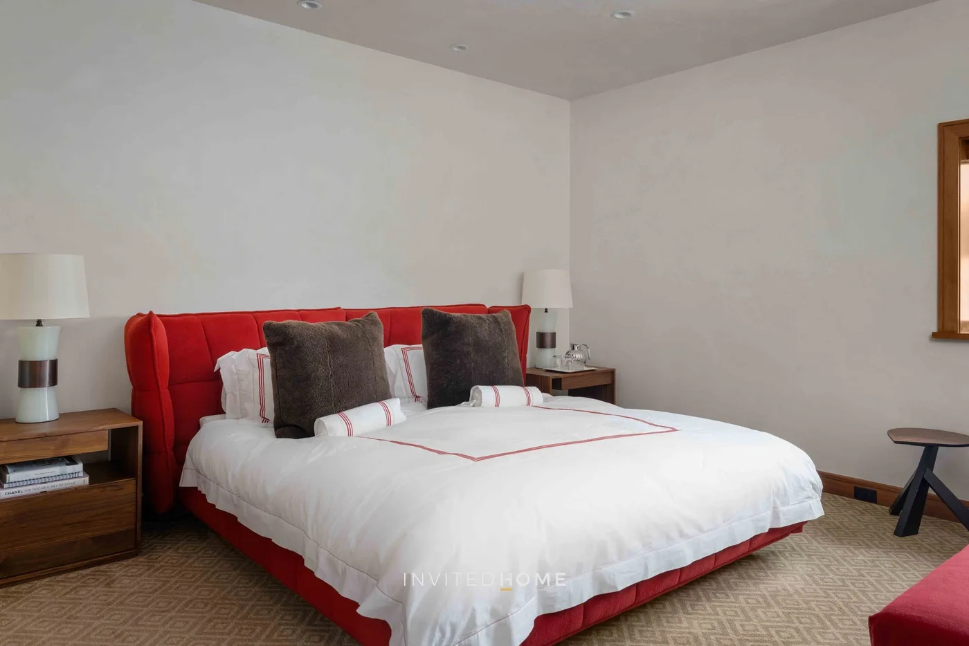 Un dormitorio con una cama roja, ropa de cama blanca y mesitas de noche.