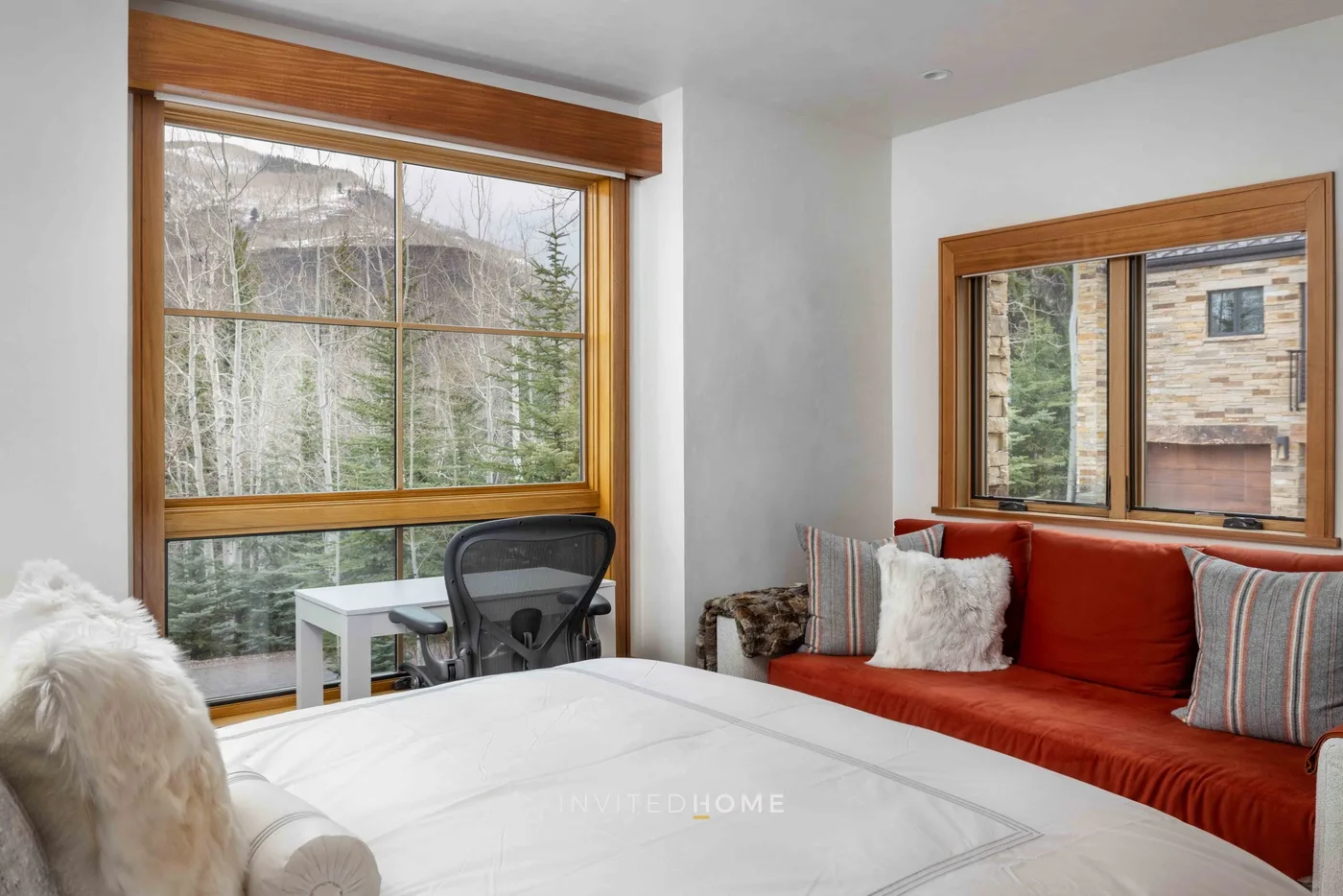 Un dormitorio con una cama junto a un sofá rojo y grandes ventanas.