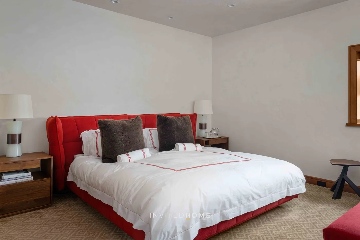 Un dormitorio con una cama roja, ropa de cama blanca y mesitas de noche.