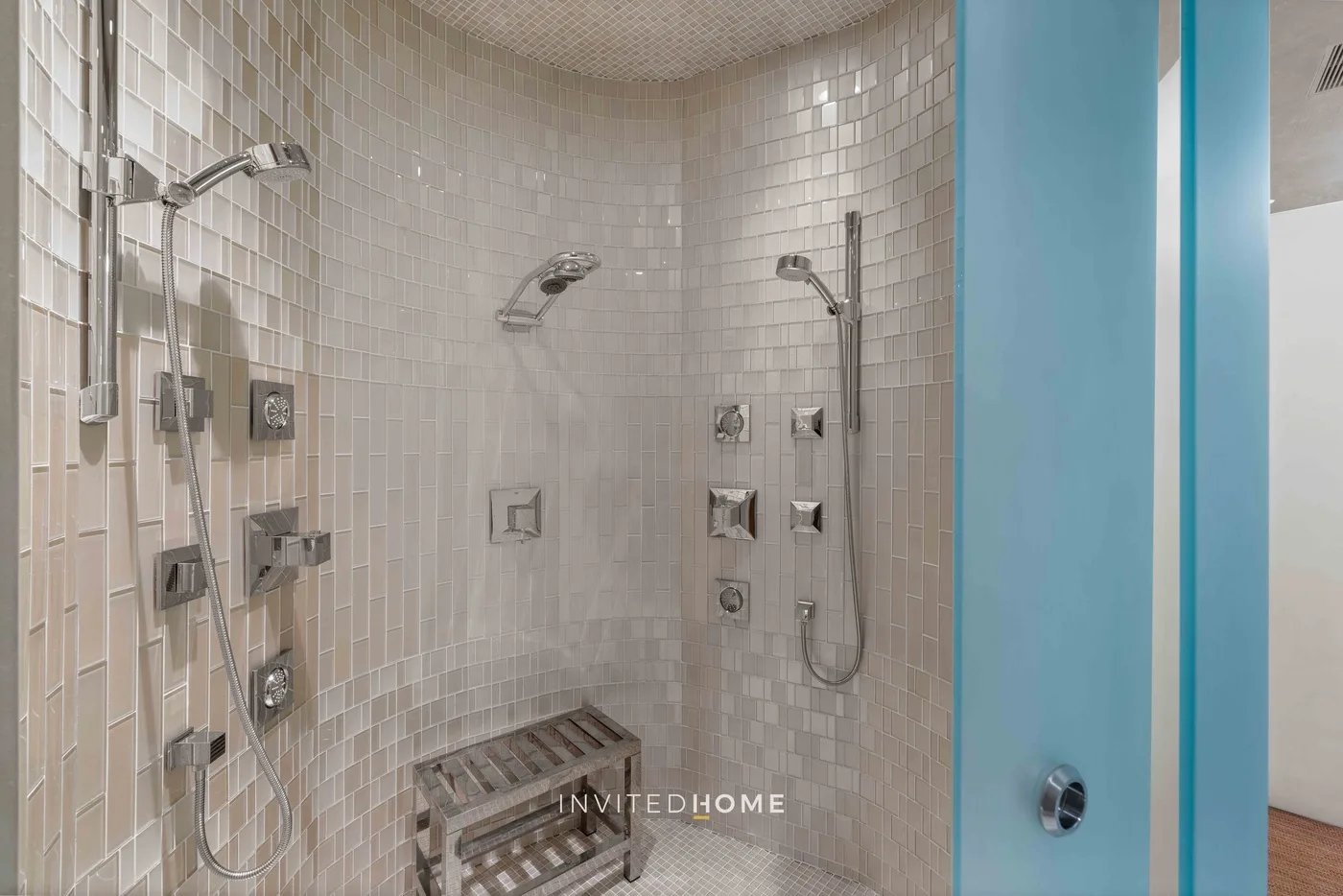 Una zona de ducha alicatada con duchas de pared y un pequeño banco de madera.