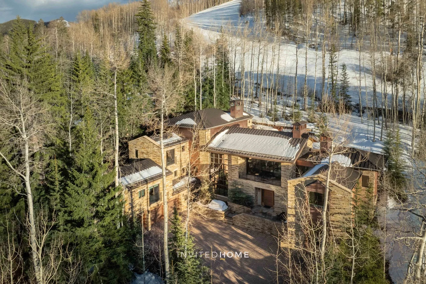 Una casa grande de madera está entre árboles junto a un paisaje nevado.