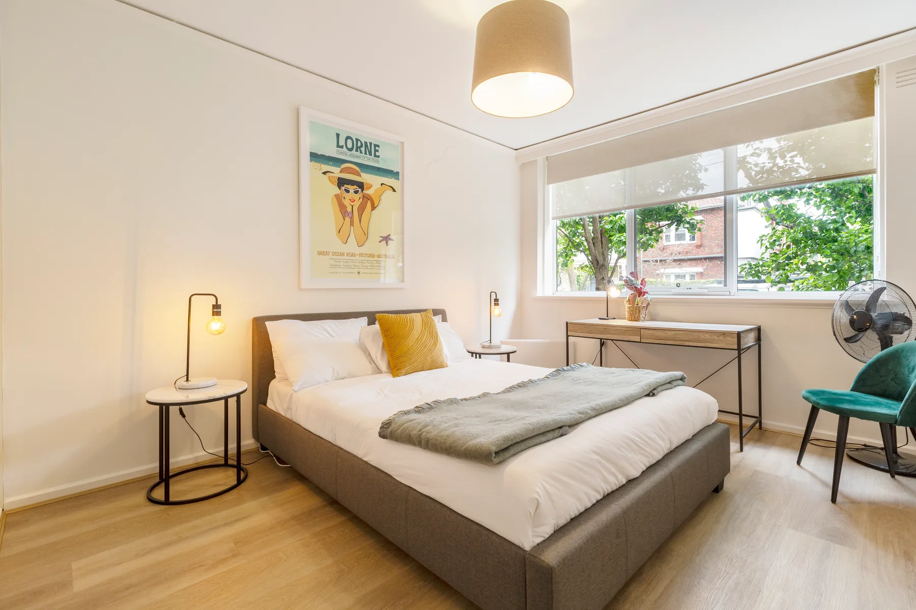 Un dormitorio luminoso tiene una cama bien tendida con una manta doblada y mesitas de noche.