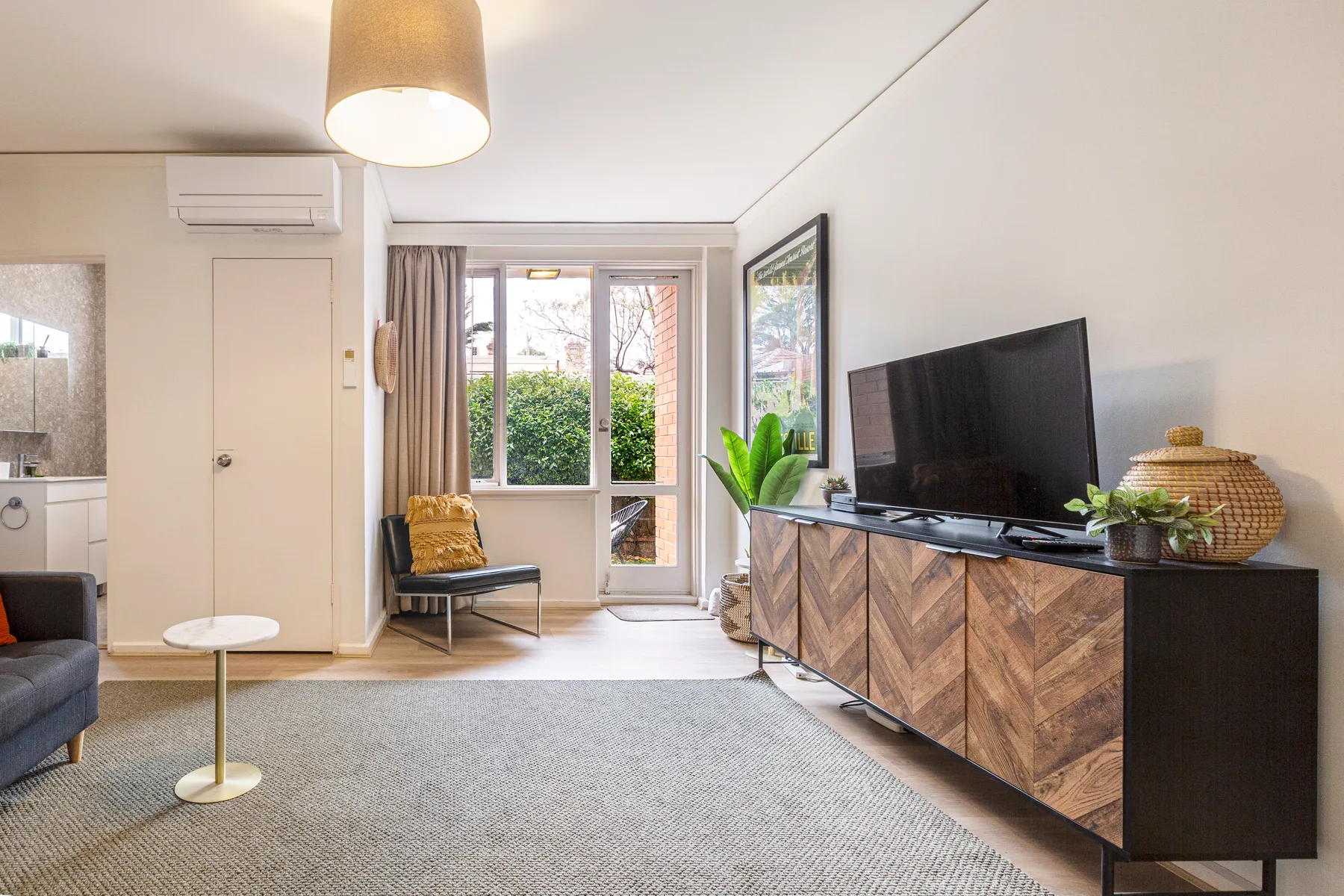 Una sala de estar con televisor, asientos y una puerta de vidrio con vista a la vegetación.