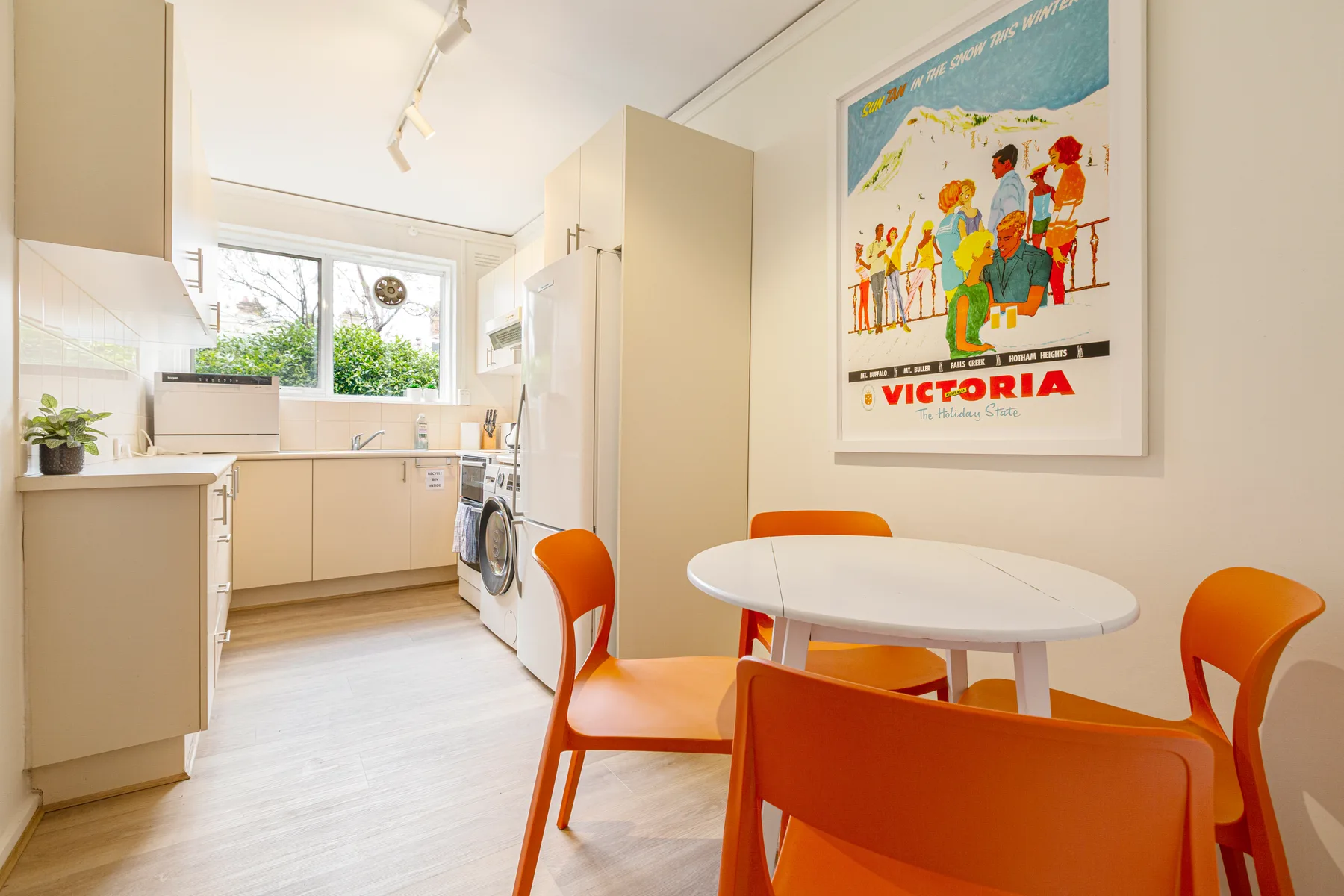 Un comedor con una mesa redonda blanca y asientos de color naranja junto a la cocina.