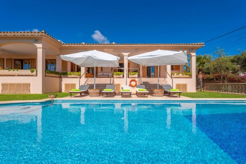 A swimming pool in front of a low building, with shaded seating along the edge.