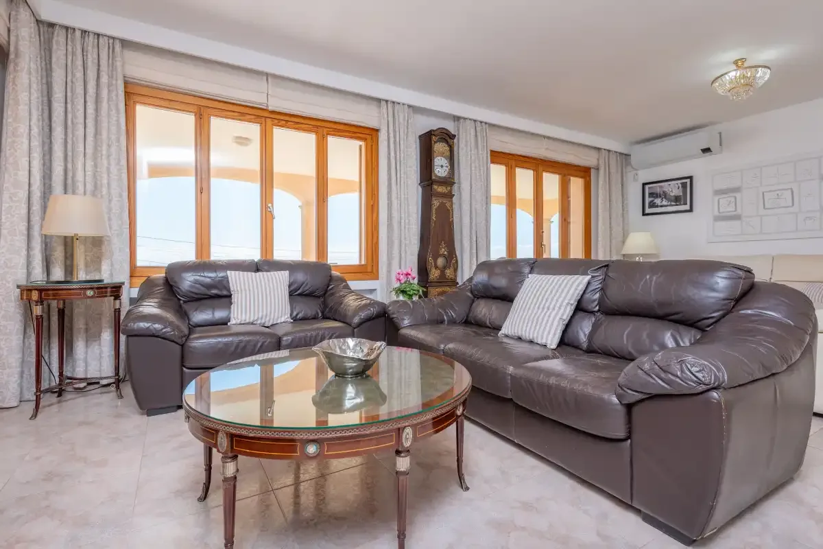A living room with leather seating, a glass coffee table, and large windows.