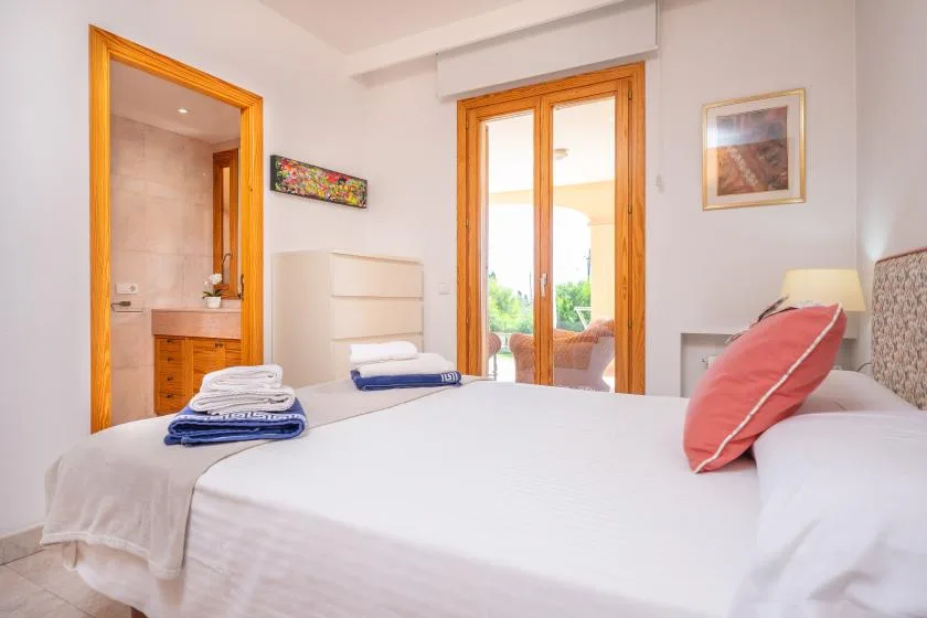 A bright bedroom with a neatly made bed and wooden-framed glass doors.