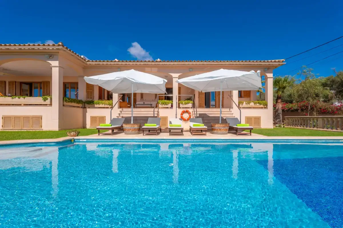A swimming pool in front of a house with loungers and umbrellas.