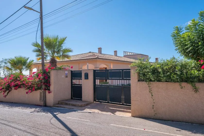 A walled residential property entrance with black metal gates and flowering shrubs.