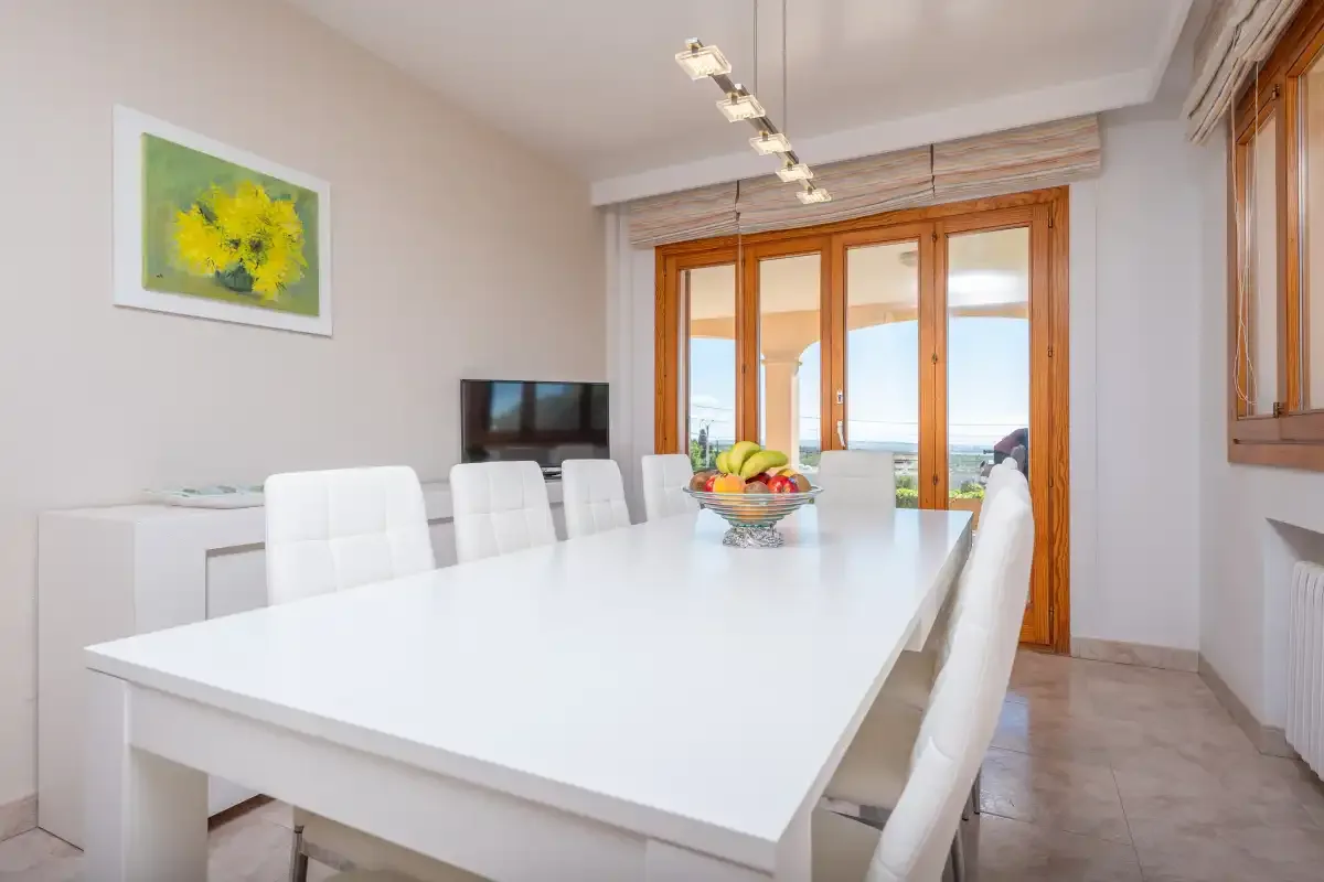A bright dining room with a long white table and large windows.