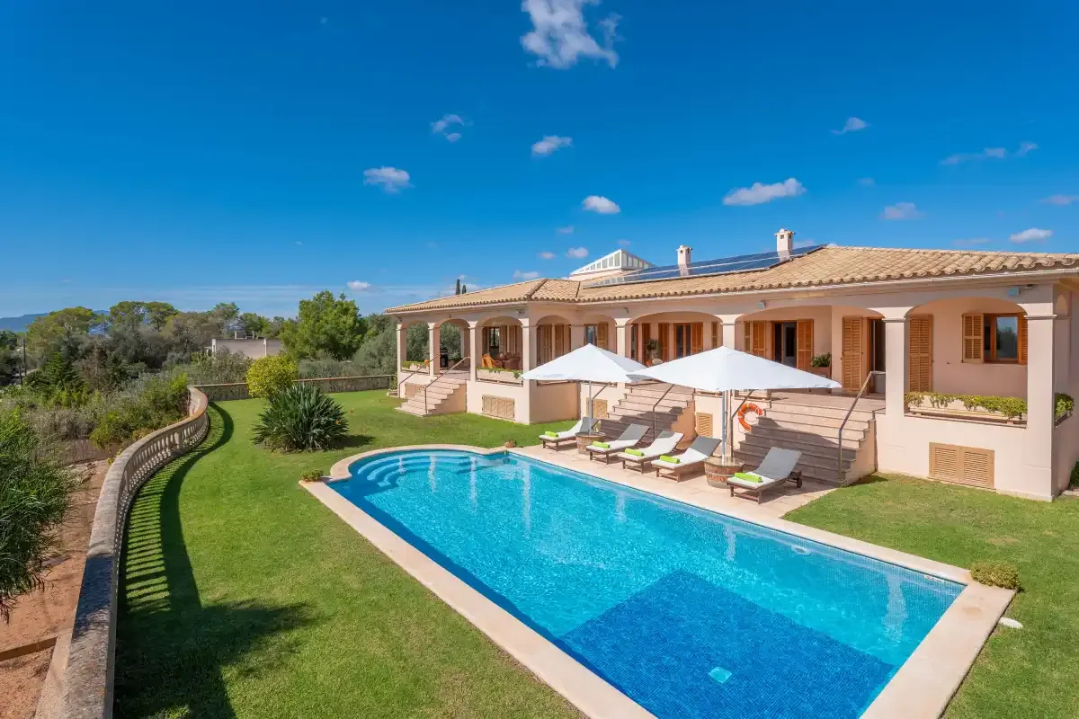 A swimming pool and lawn in front of a large villa.