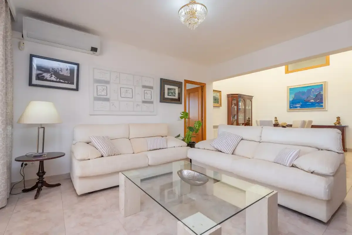 A bright living room with white seating and a glass coffee table.