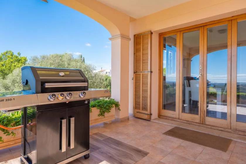 A covered patio has a built-in barbecue beside glass doors opening onto a view.