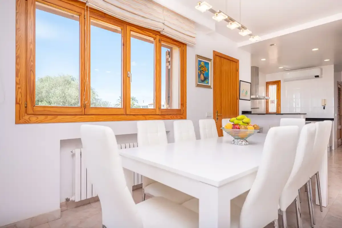 A bright dining area with a white table beside large wood-framed windows.