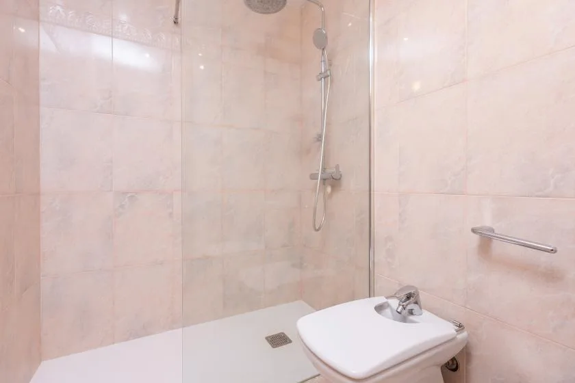 A tiled bathroom with a wall-mounted shower and a toilet.