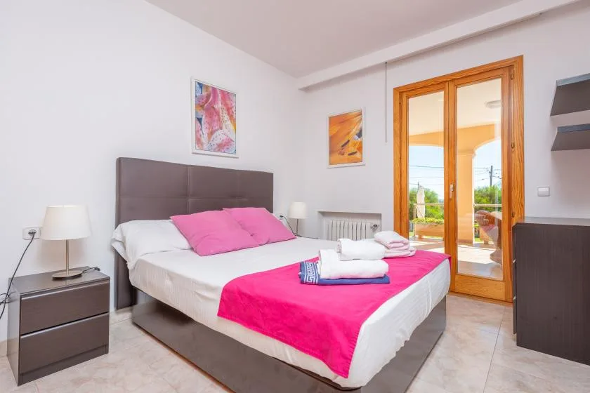 A bright bedroom with a double bed and pink bedding beside glass doors.