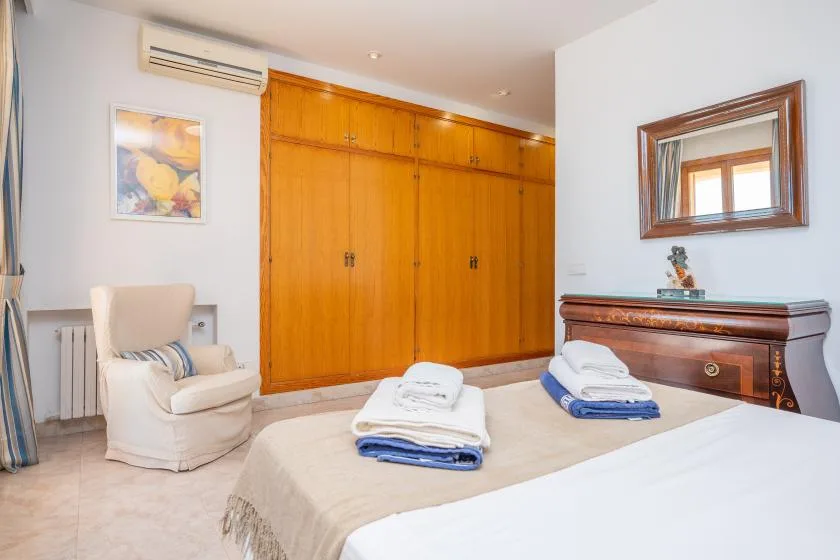 A bedroom with a bed, folded towels, and wooden wardrobes.