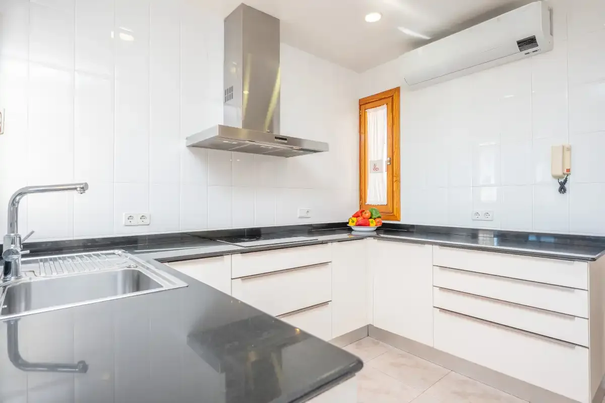 A bright kitchen with white cabinets, dark countertops, and a stainless steel range hood.