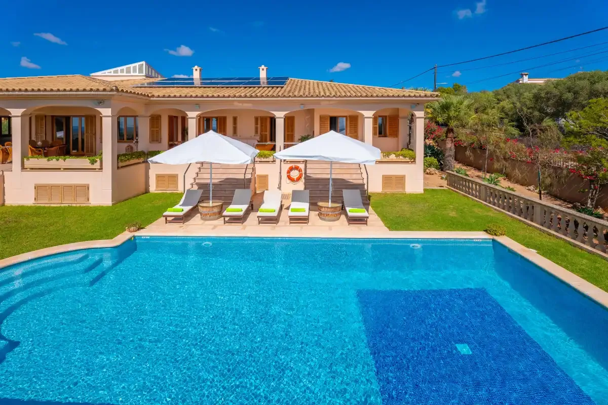A villa opens onto a swimming pool, with sun loungers arranged beside the water.