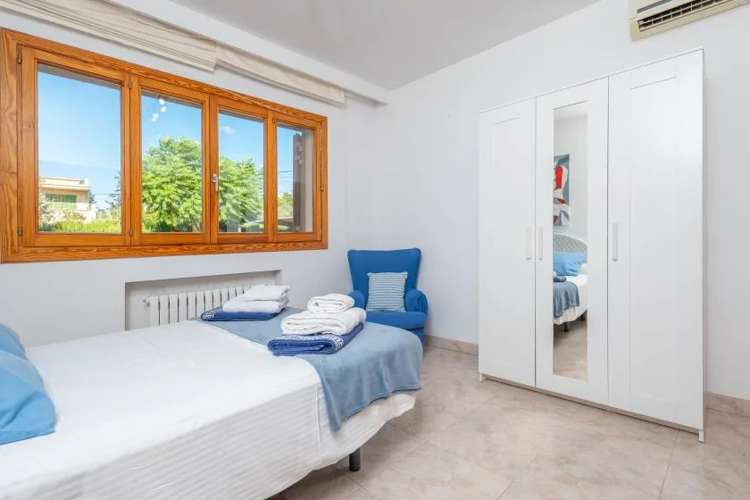 A bedroom with two beds, a blue chair, and a large wooden-framed window.