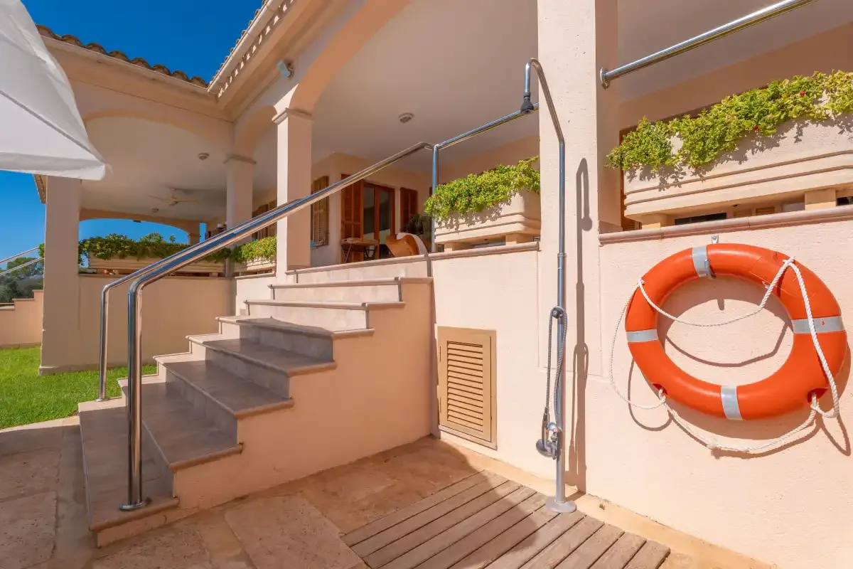 An outdoor poolside staircase with metal handrails and a lifebuoy on the wall.