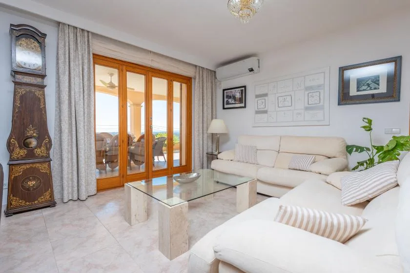 A bright living room with light-colored seating and glass doors opening onto a balcony.