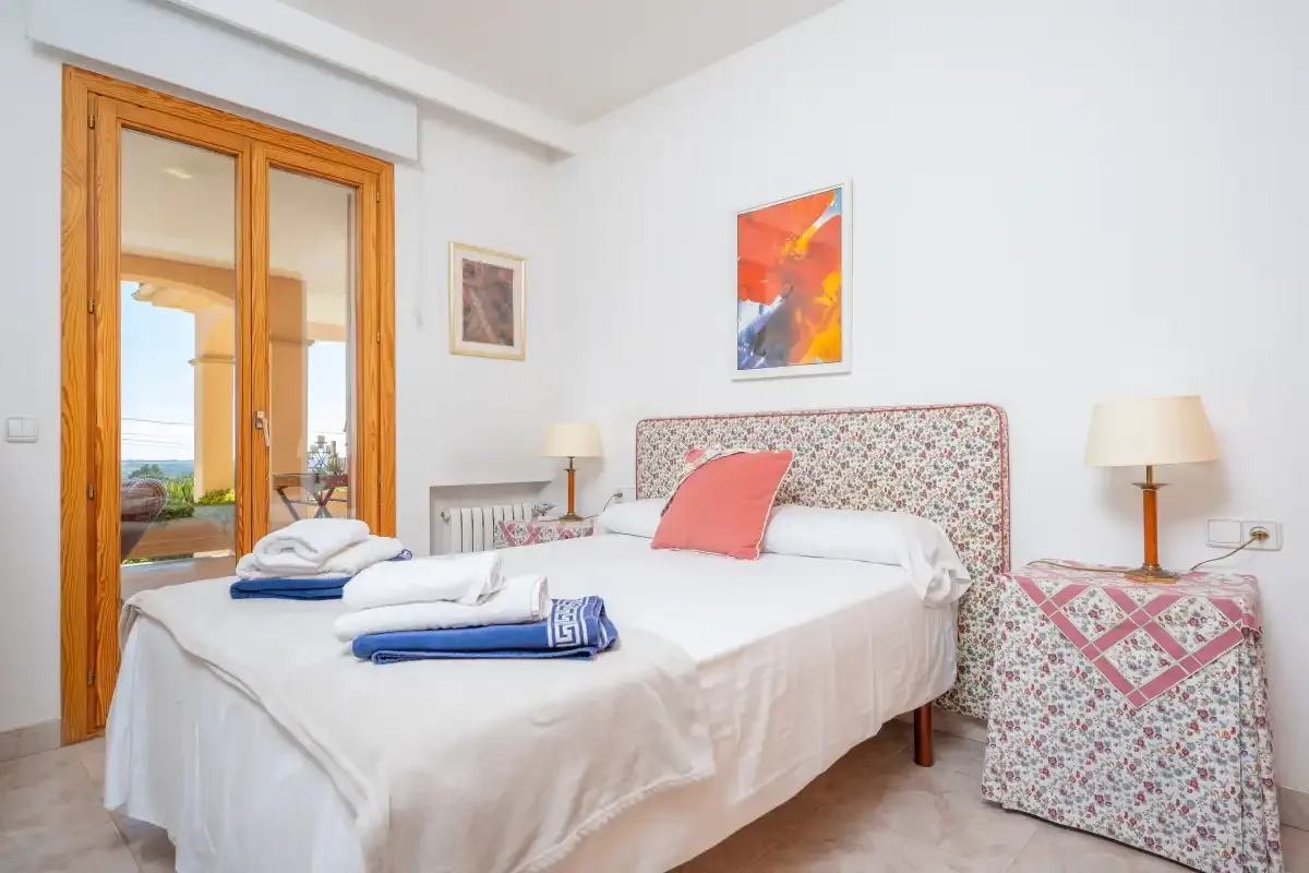 A bright bedroom with a double bed and glass doors opening onto a balcony.