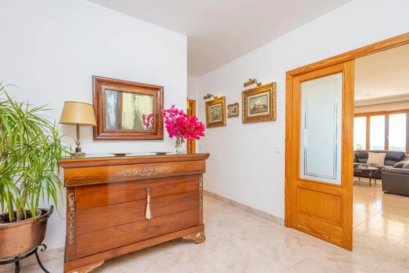 A bright hallway with a wooden chest of drawers and an open doorway to a sitting area.