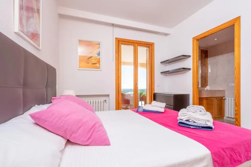 A bedroom with a bed dressed in white and bright pink linens.