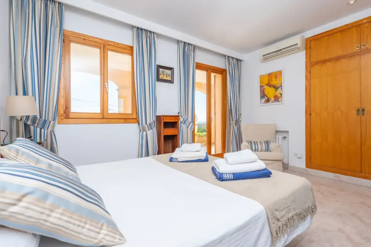 A bedroom with beds, striped curtains, and a wooden wardrobe.
