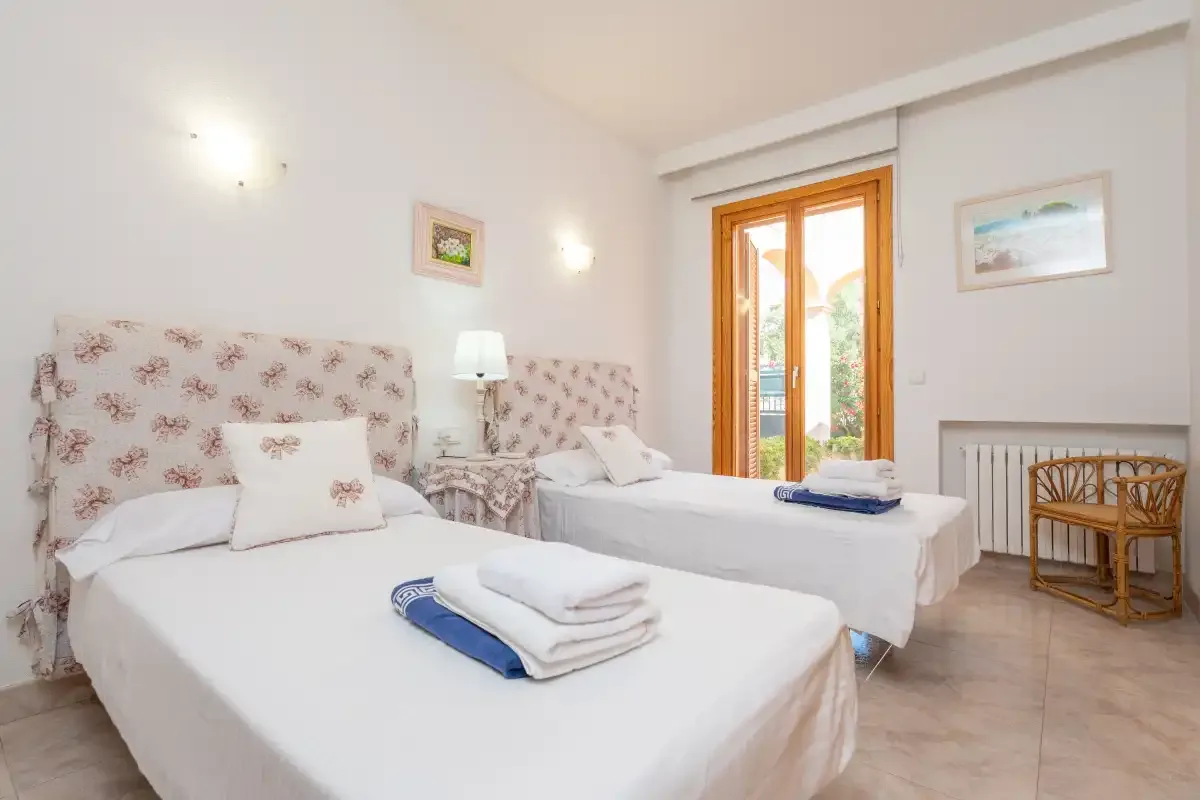 A bright bedroom with two beds, floral headboards, and a wooden-framed glass door.
