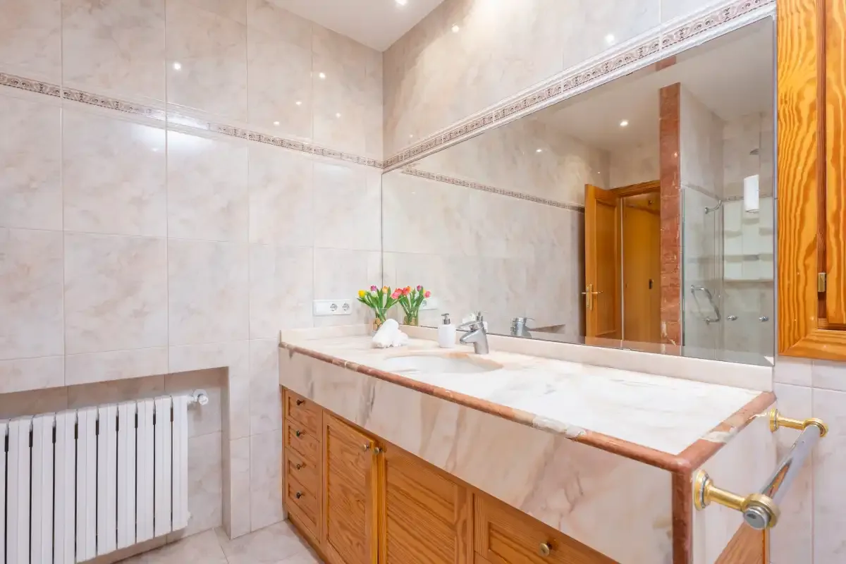 A tiled bathroom with a long vanity, mirror, and radiator.