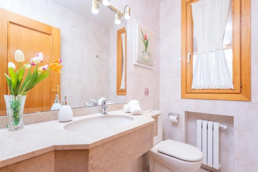 A tiled bathroom with a sink, toilet, and curtained window.