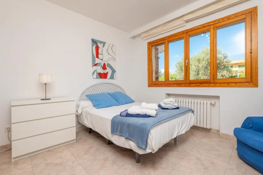 A bright bedroom with a bed, blue bedding, and a large wood-framed window.