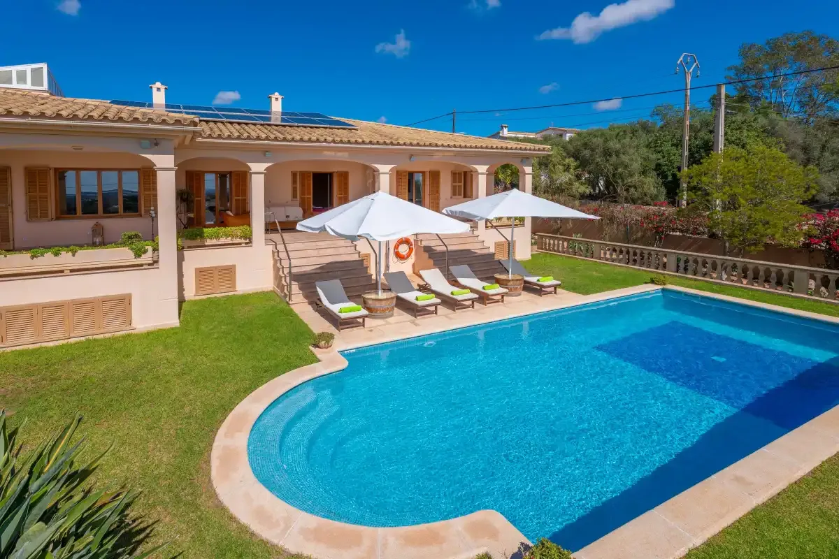A swimming pool and sun loungers sit beside a villa with a landscaped yard.