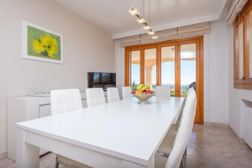 A bright dining room with a long white table and wooden-framed glass doors.