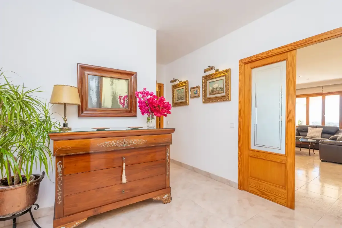 A bright hallway with a wooden chest and an open doorway to a sitting area.