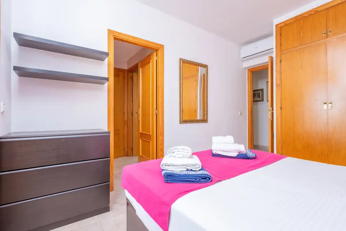 A bedroom with a bed dressed in bright pink and blue linens.