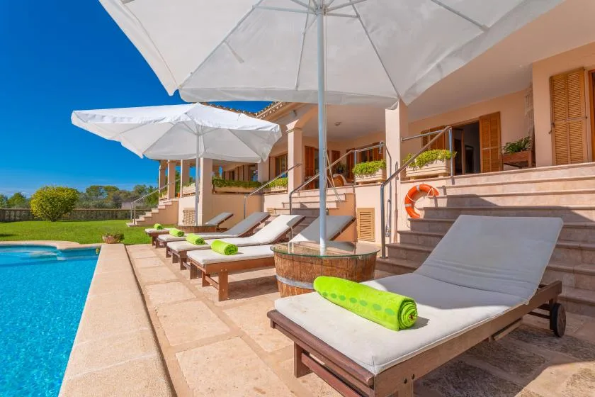 Outdoor poolside lounge with cushioned sun loungers and large white umbrellas.