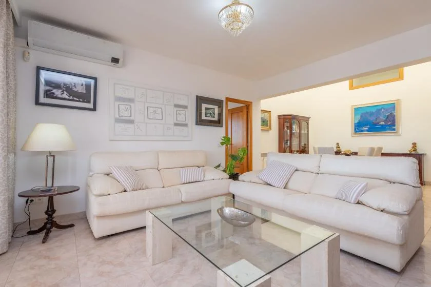 A bright living room with pale seating and a glass coffee table.
